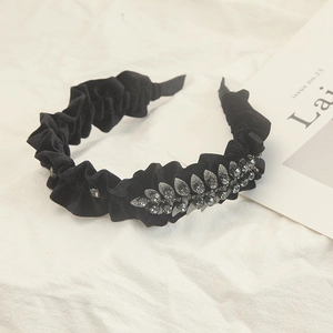 Close-up of black pleated velvet headband featuring elegant rhinestone leaf detailing