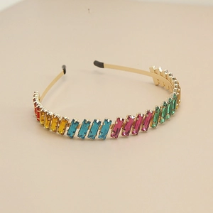 Close-up of golden metal headband with colorful rectangular rhinestones on beige background