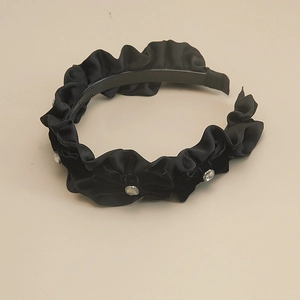 Détail d'un serre-tête plissé noir avec un nœud en velours et un cristal étincelant