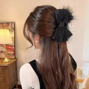 Detail view of a large black bow hair claw clip with fluffy ostrich feathers on model