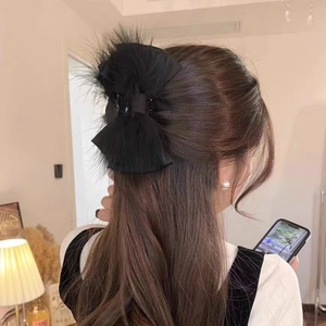 Back view of a woman wearing a large black velvet bow hair claw with ostrich feathers