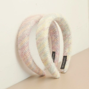 Détail de deux serre-têtes tressés en peluche faits main aux rayures arc-en-ciel pastel