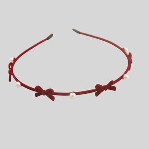 Close-up of velvet red headband with white pearls and bow ties on a slim frame