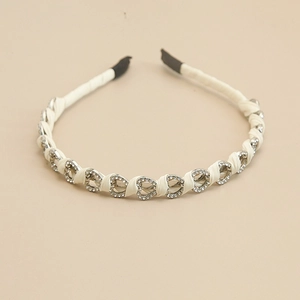 Dettaglio di strass a forma di cuore su cerchietto in raso crema con montature in metallo
