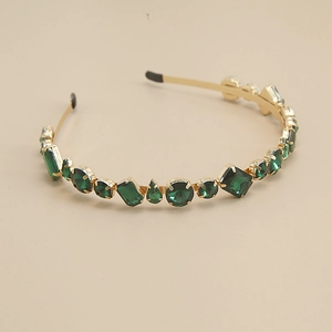 Détail d'un serre-tête doré orné de strass vert émeraude de formes et tailles variées