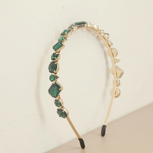 Détail d'un serre-tête en métal doré orné de strass vert émeraude aux formes géométriques