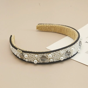 Elegant wide pearl and gray crystal headband with LOVEDAYS gold charm on beige background