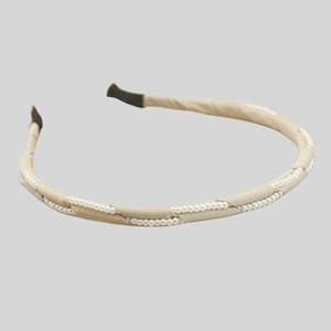 Detail of elegant champagne satin headband featuring rows of white imitation pearls