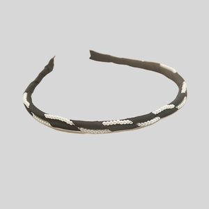 Close-up of black fabric headband with elegant white pearl woven design for women
