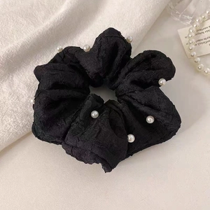 Détail d'un chouchou noir texturé avec perles blanches sur un fond en tissu esthétique