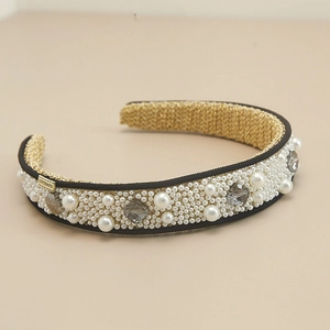 Detailed macro view of retro headband with white pearls, crystals, and gold branding plate