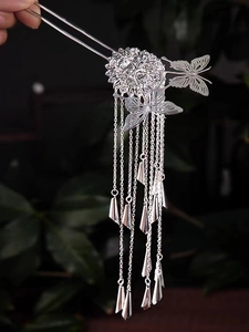 Detail of silver butterfly hair pin with cascading metallic tassels and hollow floral base