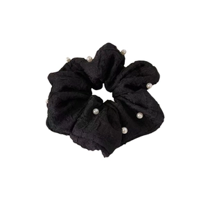 Chouchou plissé noir élégant avec des perles blanches sur un fond blanc immaculé