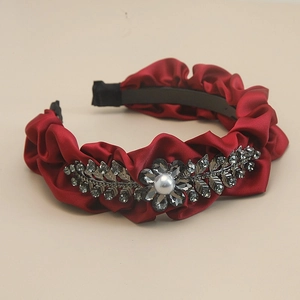 Detailed macro view of burgundy pleated satin headband with crystal leaf and pearl accents