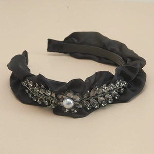 Detailed close-up of rhinestone leaves and pearl on black pleated satin headband