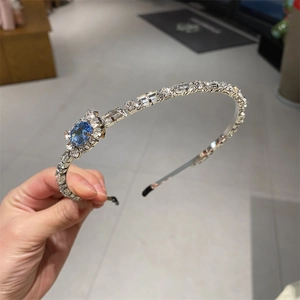 Close-up of thin silver headband featuring blue oval crystal and white rhinestone floral detail