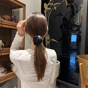 Dettaglio di un elastico per capelli a rosa in raso nero indossato su una coda di cavallo