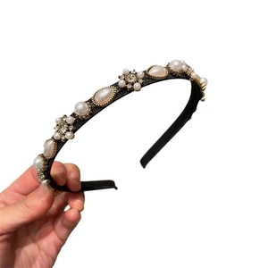 Elegant black headband with faux pearls and rhinestones shown in hand against white background