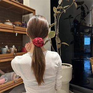 Dettaglio di uno scrunchie a rosa in seta rossa su una coda di cavallo bassa