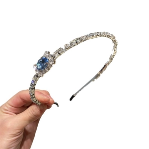 Elegant silver metal headband with clear crystals and a large blue oval rhinestone