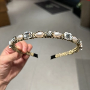Dettaglio del cerchietto vintage con perle e cristalli su tessuto intrecciato oro