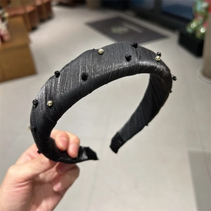 Détail du serre-tête large en tissu orné de perles noires et dorées avec fil métallique brillant