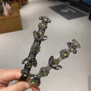 Detail showing crystal leaf headband with green stones and crossed C brand logo