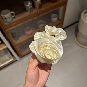 Primo piano di un elastico per capelli in raso crema a forma di rosa tenuto in mano