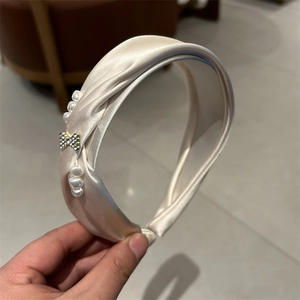 Detail view of champagne satin headband with pearls and sparkling rhinestone bow ornament