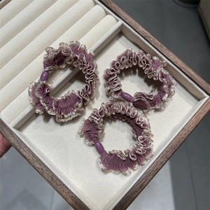 Détail de trois chouchous violets avec bords dorés et perles ovales dans une boîte