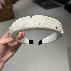 Gros plan sur le serre-tête en tissu beige avec cristaux clairs et perles dorées