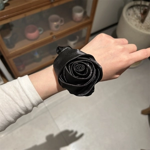 Dettaglio di un elastico per capelli a rosa in raso nero al polso, con morbidi petali floreali