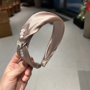 Detail of champagne satin twist headband with elegant pearls and rhinestone bow charm