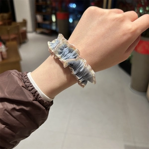 Chouchou plissé bleu avec bordure dorée métallique porté au poignet pour un look élégant
