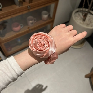 Vista dettagliata di un elastico per capelli in raso rosa a forma di rosa indossato al polso