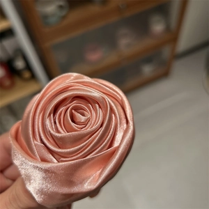 Dettaglio dell'elastico per capelli con rosa in raso corallo e petali in tessuto