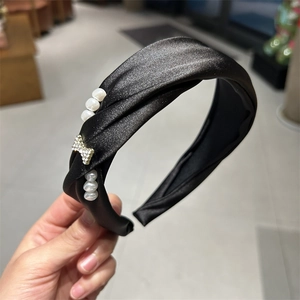 Detail of black satin knotted headband featuring white pearls and a crystal bow accent
