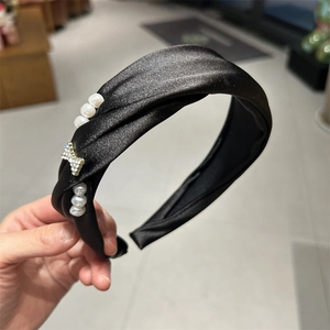 Detail of black satin twisted headband with white pearls and rhinestone bow accessory