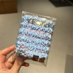 Detail view of pastel blue and pink ruffled scrunchies with pleated texture in a clear box