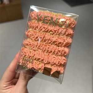 Detail view of pink pleated hair ties in a clear plastic box with elegant gold text