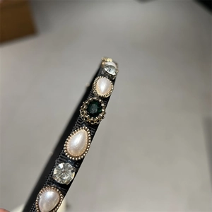 Detailed close-up of a pearl and emerald headband with crystal inlay on a black band