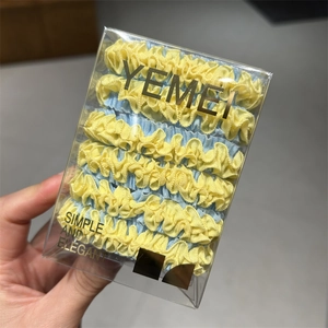 Detail view of yellow and light blue pleated hair ties in a clear square gift box