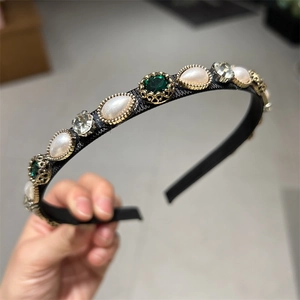 Detailed close-up of retro headband with green gems, pearls and rhinestones on black silk