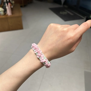 Detail of pink and light green pleated fabric scrunchie with wavy edges worn on wrist