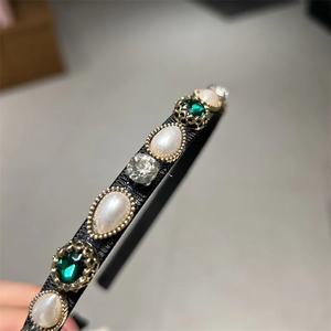 Detail of vintage headband featuring emerald gems, white pearls, and clear rhinestones