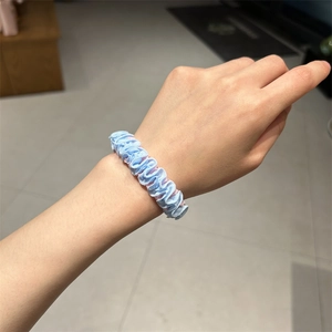 Detail shot of a light blue pleated hair tie showing elastic fabric and pink lining