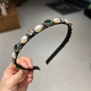 Detailed view of black headband with gold frame, white pearls and green rhinestones