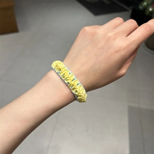 Close-up of yellow and blue ruffled hair scrunchie worn on a wrist for daily use