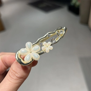 Gros plan détaillé d'une pince à cheveux dorée avec fleurs blanc nacré et cristaux brillants