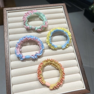 Detail of four pleated macaron hair scrunchies with decorative oval beads in a display tray